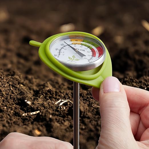 Hand holding a green soil thermometer in soil